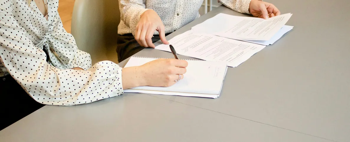 Toplantı masasında belgeleri ve notları birlikte inceleyen iki kişi