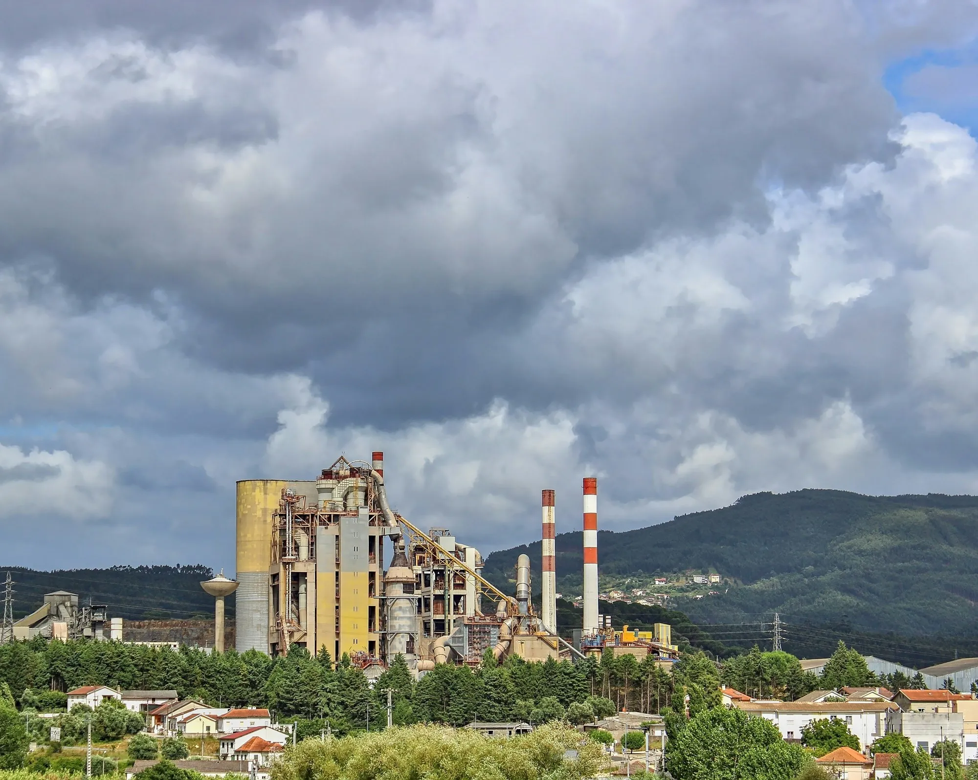 Bulutlu gökyüzü altında çimento fabrikası, silolar ve bacalar