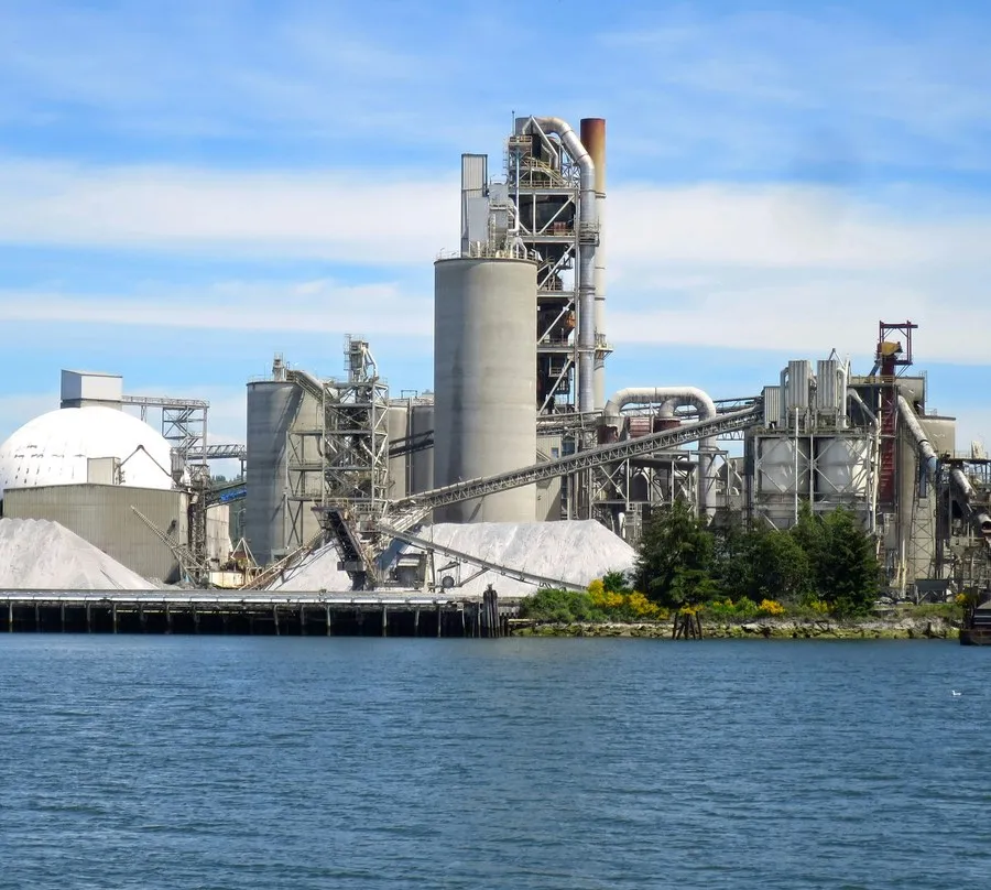 Kıyıdaki çimento fabrikasında silolar, bantlı konveyör ve hammadde yığınları